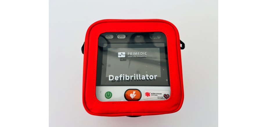 Eine rote, quadratische Tasche mit Sichtfenster zeigt einen Defibrillator von PRIMEDIC.