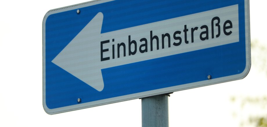 Es ist ein Straßenschild abgebildet blau mit weißem Pfeil nach links mit den Worten Einbahnstraße