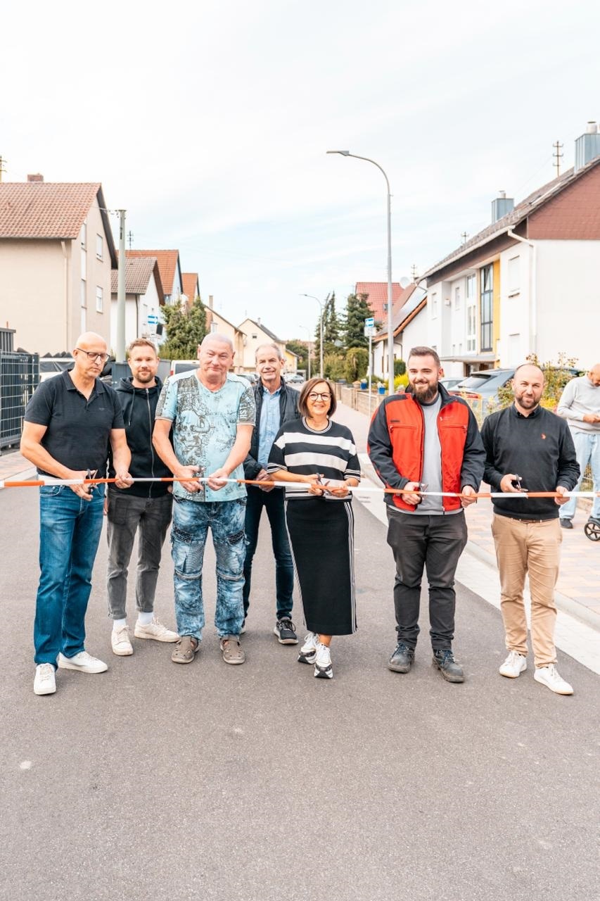 Abgebildet sind 6 Männer und 1 Frau die auf der Straße stehen und ein Band durchschneiden.